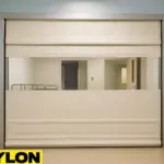A beige Roll-Up Vinyl Door manual, installed in a healthcare facility hallway, separating a clean patient zone with visible hospital equipment through a clear vinyl window