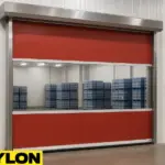 Roll-Up Vinyl Door – Motorized by Paylon, shown in red with a wide vision panel, installed in a clean storage facility with stacked water bottle pallets