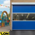 Roll-Up Vinyl Door Motorized installed at a theme park facility entrance, with colorful roller coasters and fencing in the background