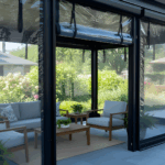 “Black-frame pavilion with roll-up clear vinyl curtains partially raised, showing a modern outdoor seating area protected from wind and weather.”