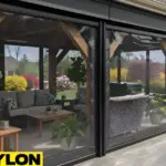 Motorized clear vinyl pavilion curtains in a black frame enclosure, showcasing a protected outdoor seating area with clear views of the yard.