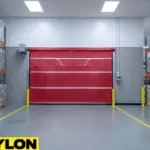 Red high-speed vinyl roll-up door installed in a warehouse aisle with pallet racks and safety bollards.