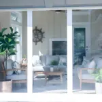 “White-framed motorized clear vinyl curtains enclosing a sun room, demonstrating protection from element while allowing natural light.”