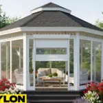 “White roll up vinyl door installed on a backyard gazebo with clear side panels, surrounded by colorful garden flowers.”