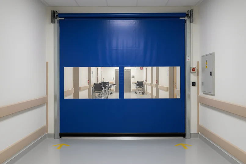 Blue roll-up vinyl door with vision panels in a healthcare corridor, supporting visibility and smooth movement between care zones.