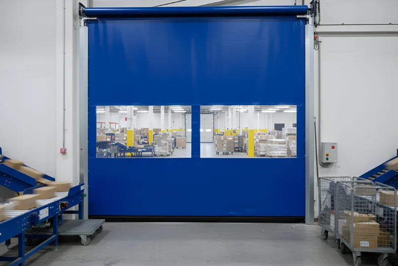 Interior roll-up vinyl door connecting warehouse work areas with frequent employee and equipment traffic