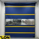 Motorized blue vinyl roll-up door with yellow stripes separating storage and production areas in a winery facility.
