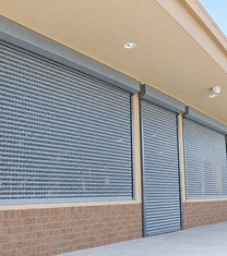 Perforated vented roll-up security doors closed over shop windows and an entry door on a tan storefront