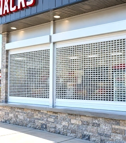 Roll-up storefront grid door closed over a retail shop window, keeping the display visible while blocking entry.